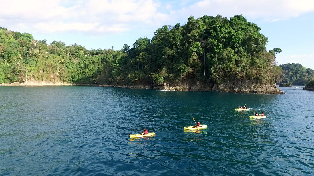 Kayaks on the calm blue bay below a jungle-covered island in Manuel Antonio