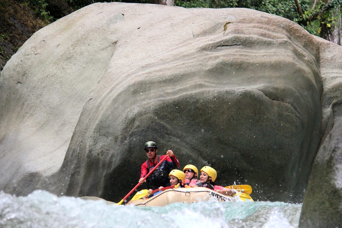 A family raft passing under a huge boulder on El Chorro