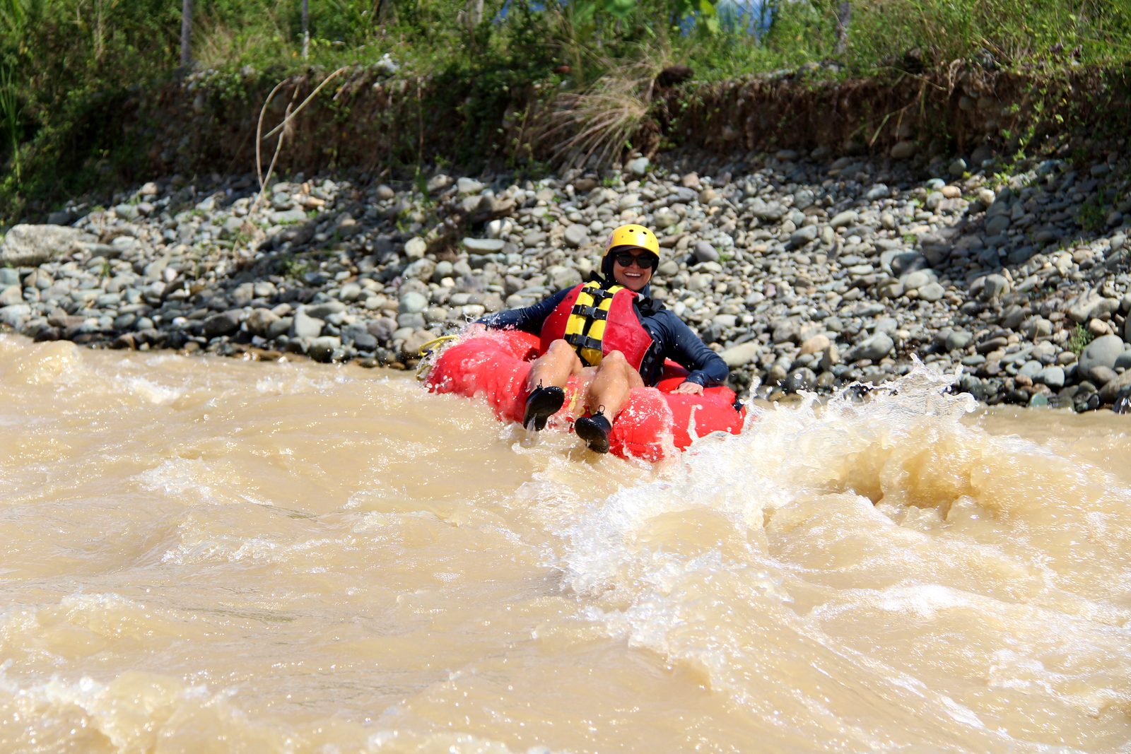 A guest bounces through a splash in her tube below a rocky bank