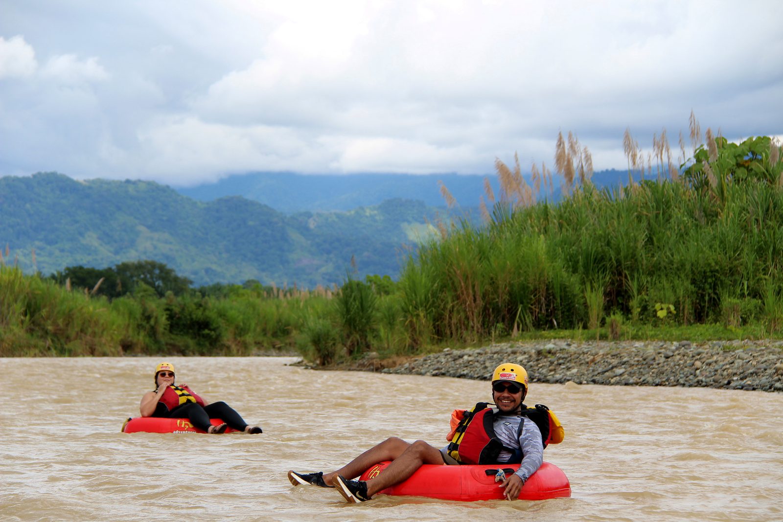 Two guests relax in their tubes by tall cane on the bank